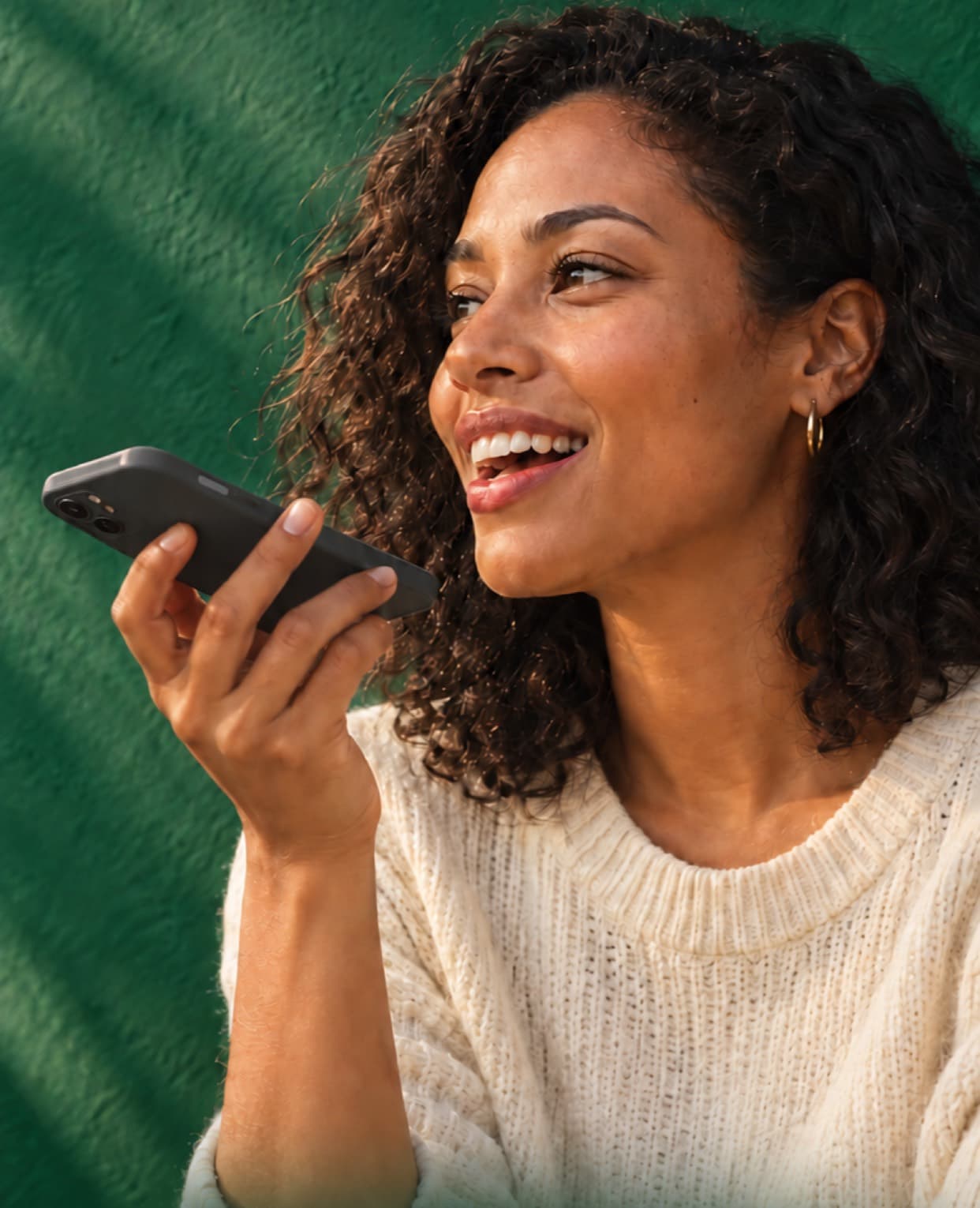 A woman laughing as she speaks into her phone in front of a green wall